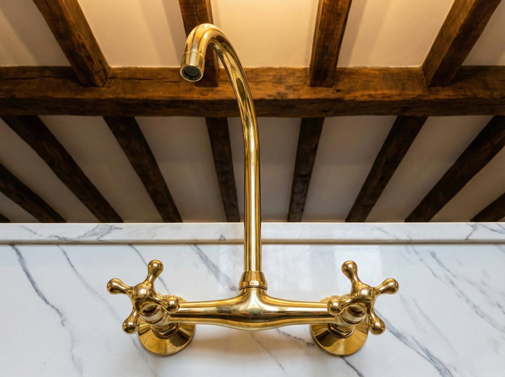 Gold kitchen faucet on a marble countertop with wooden beams in the background