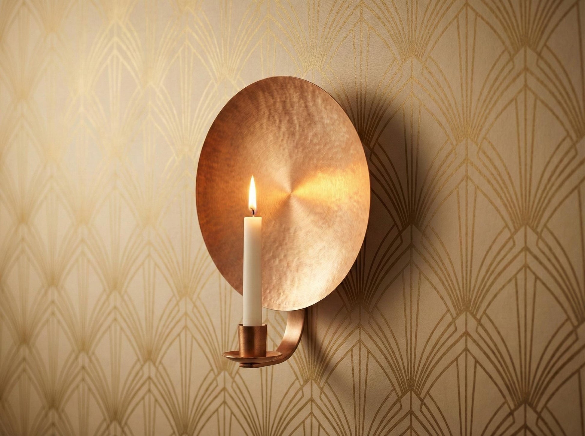 Copper wall sconce with a lit candle on a patterned wall
