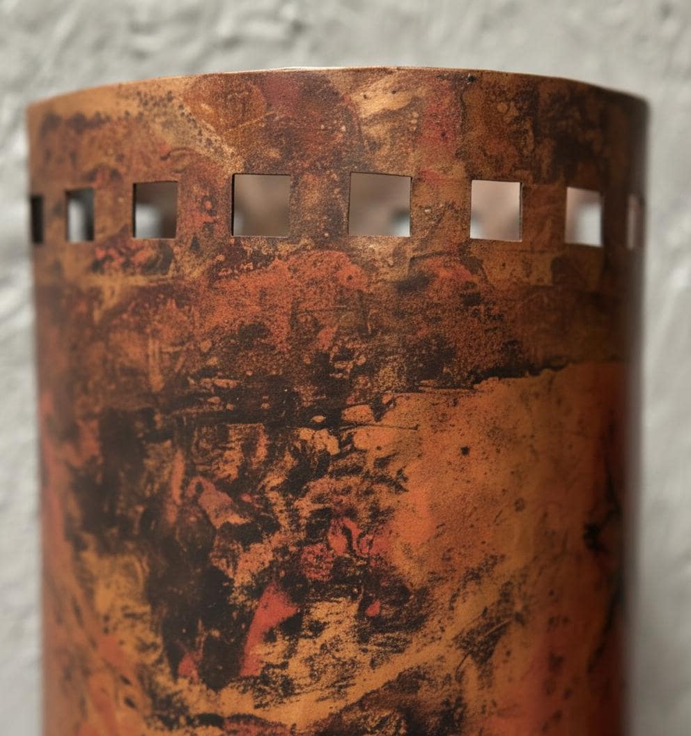 Cylindrical metal object with textured surface and cut-out patterns on a gray background