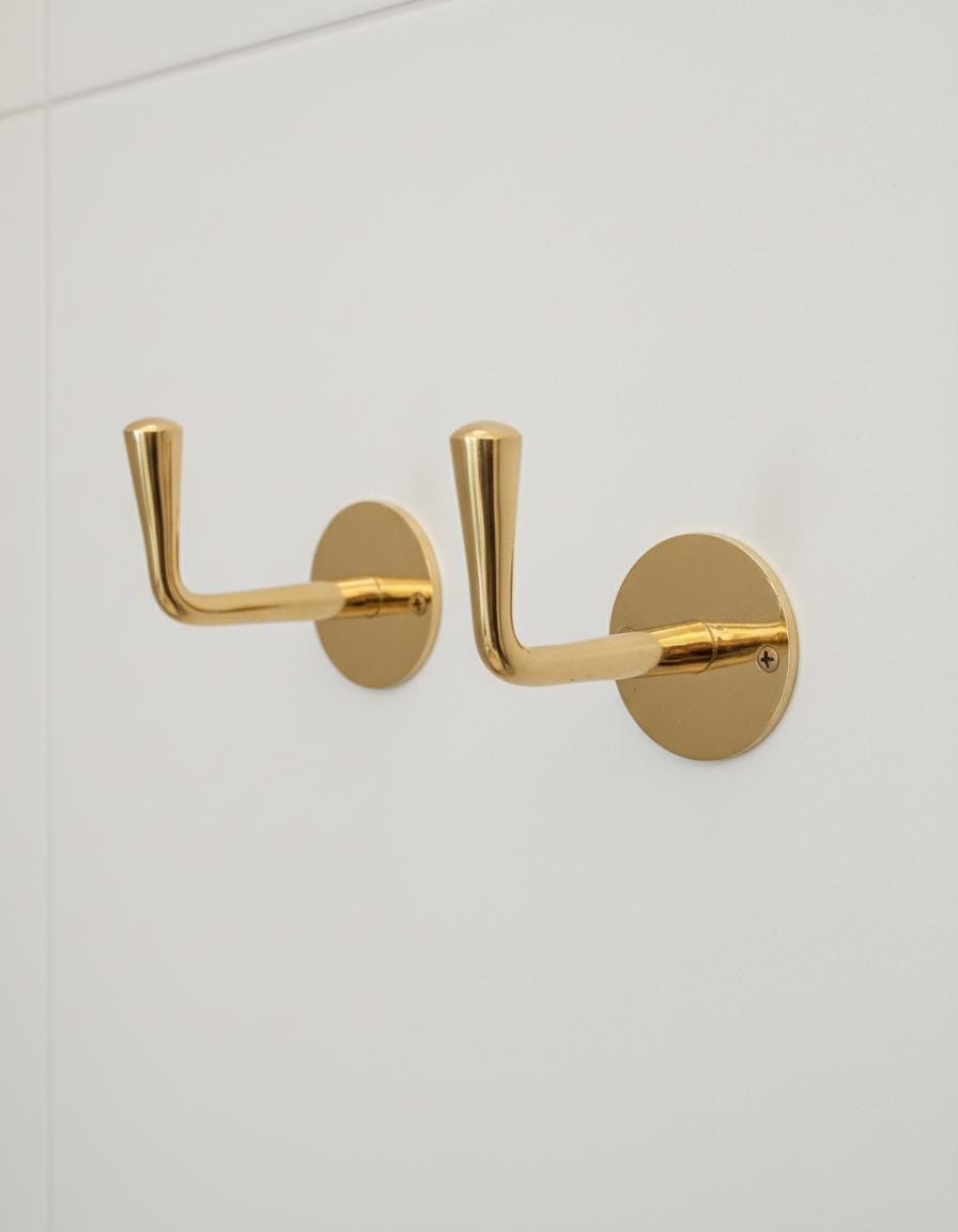Two gold hooks on a white wall