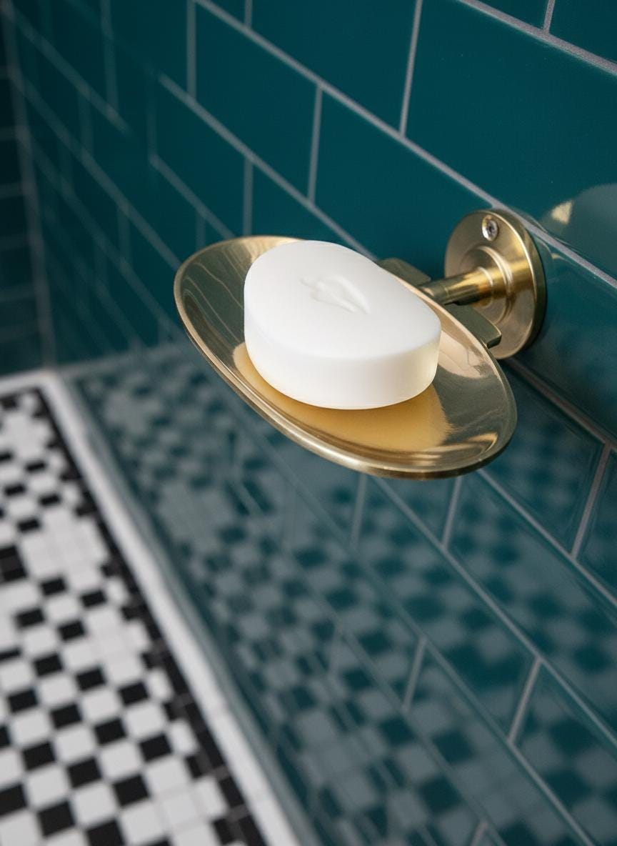 Gold soap dish with a bar of soap against a green tiled bathroom wall.
