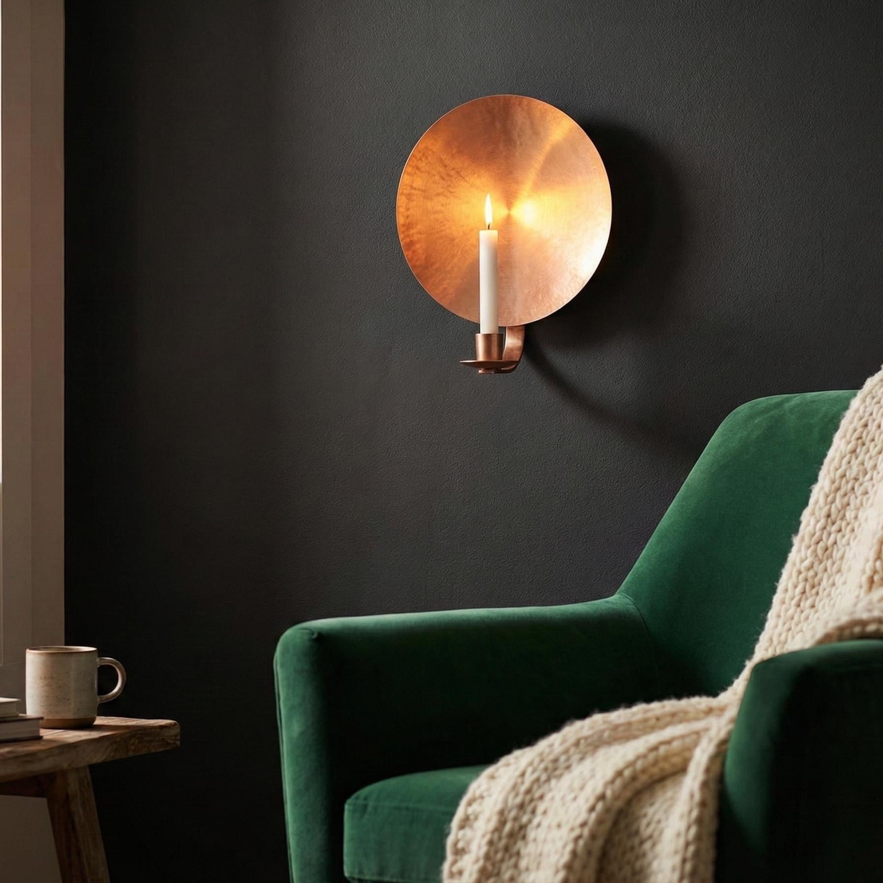 Green armchair with a blanket and a wall-mounted copper light fixture in a dark room.