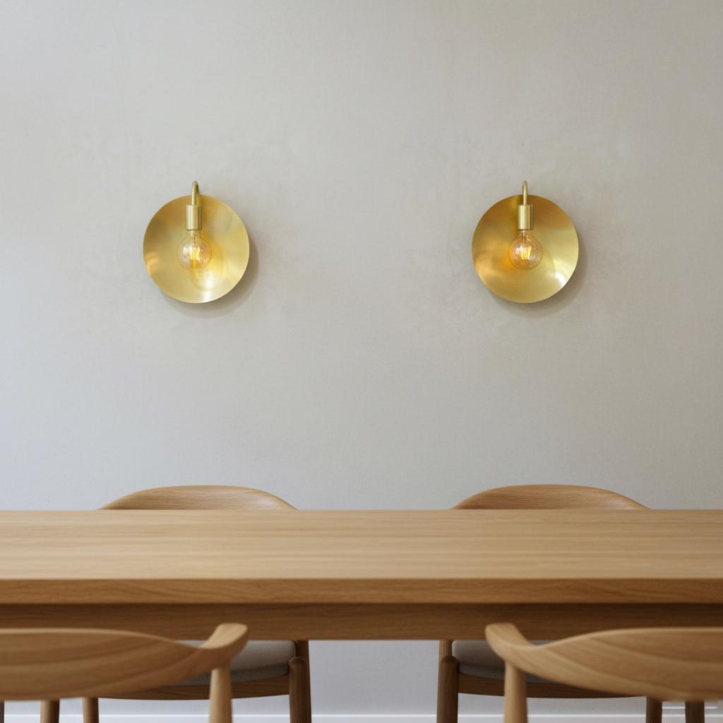 Modern dining room with wooden table and chairs, and two gold wall sconces on a light gray wall.