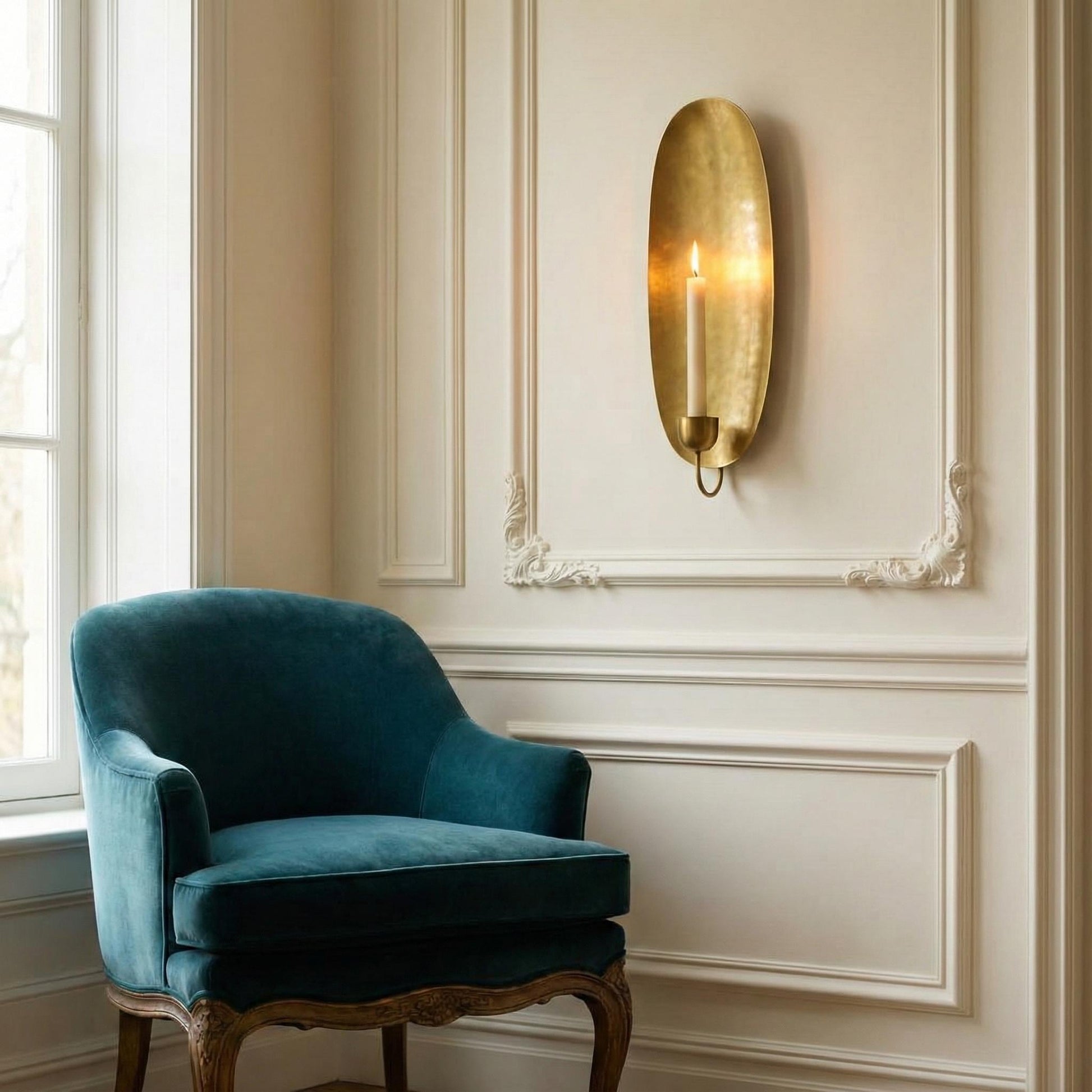 Blue velvet chair in a room with decorative wall molding and a gold wall sconce.