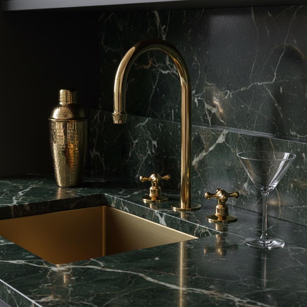 Gold faucet and sink on a dark marble countertop with a cocktail shaker and glass.