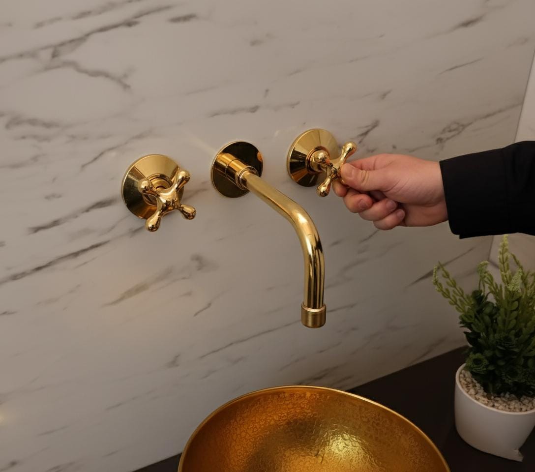 Gold faucet being turned by a hand against a marble wall.
