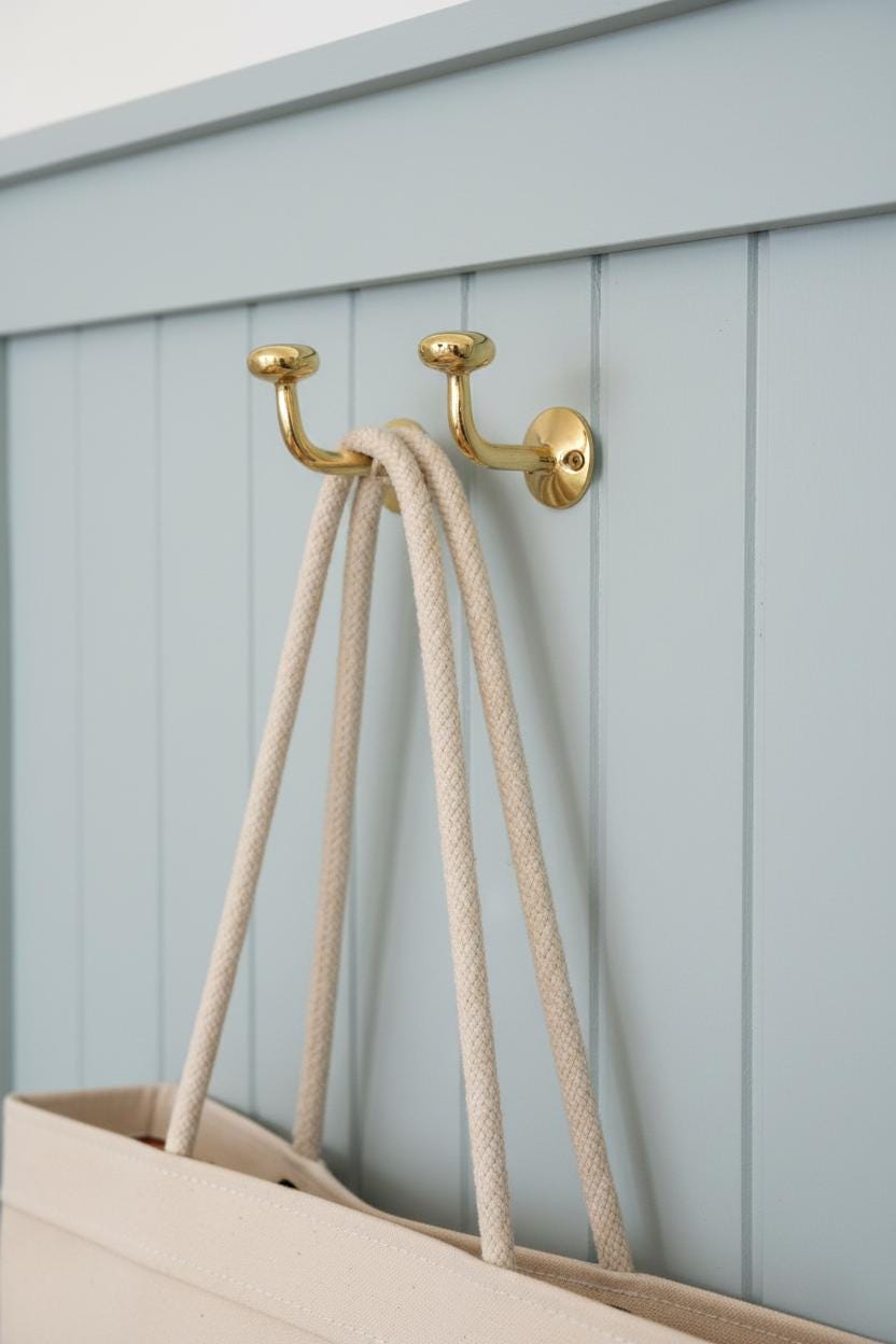 Gold hooks on a light blue wooden panel with a beige tote bag hanging from them.