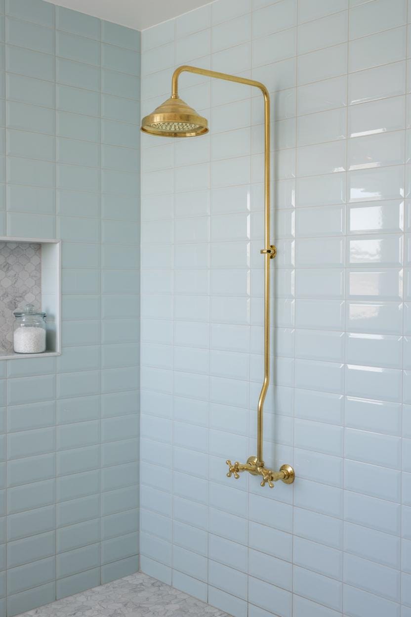 Gold shower head and fixtures against light blue tiled walls in a bathroom.
