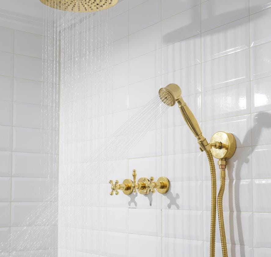 Gold shower head and control handle mounted on a white tiled wall.