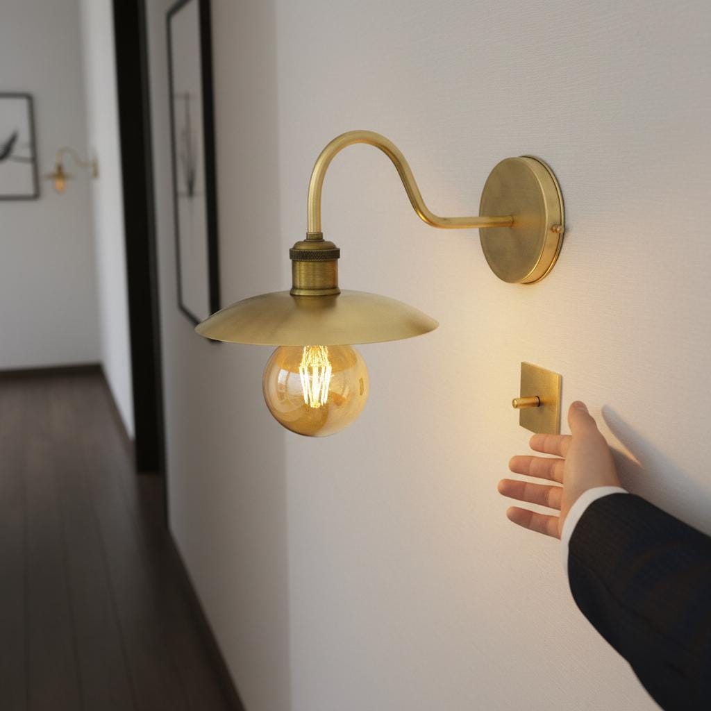 Brass wall-mounted light fixture with a glowing bulb on a gray background