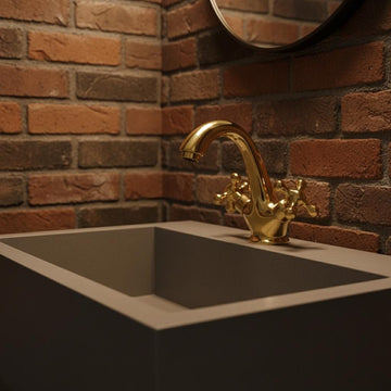 Gold faucet on a sink with a brick wall background