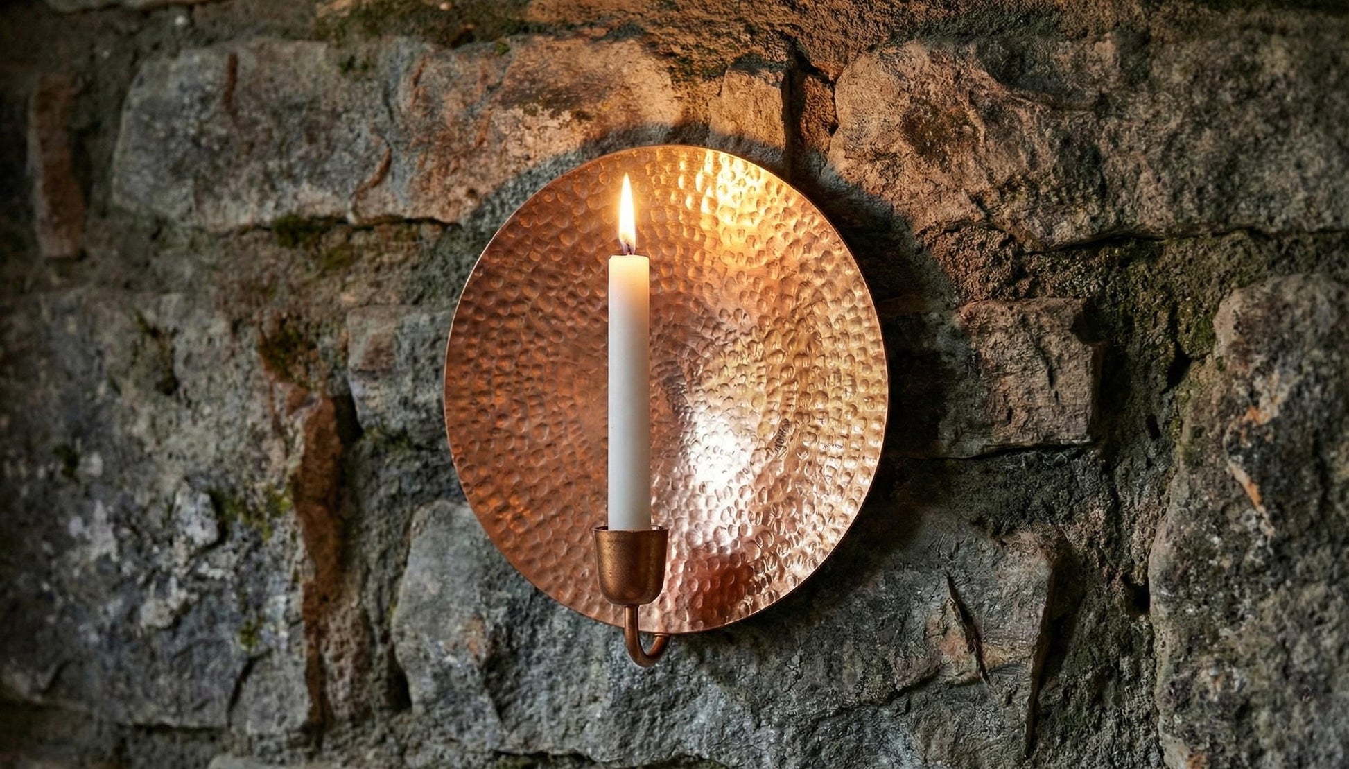 Copper wall sconce with a candle on a stone wall