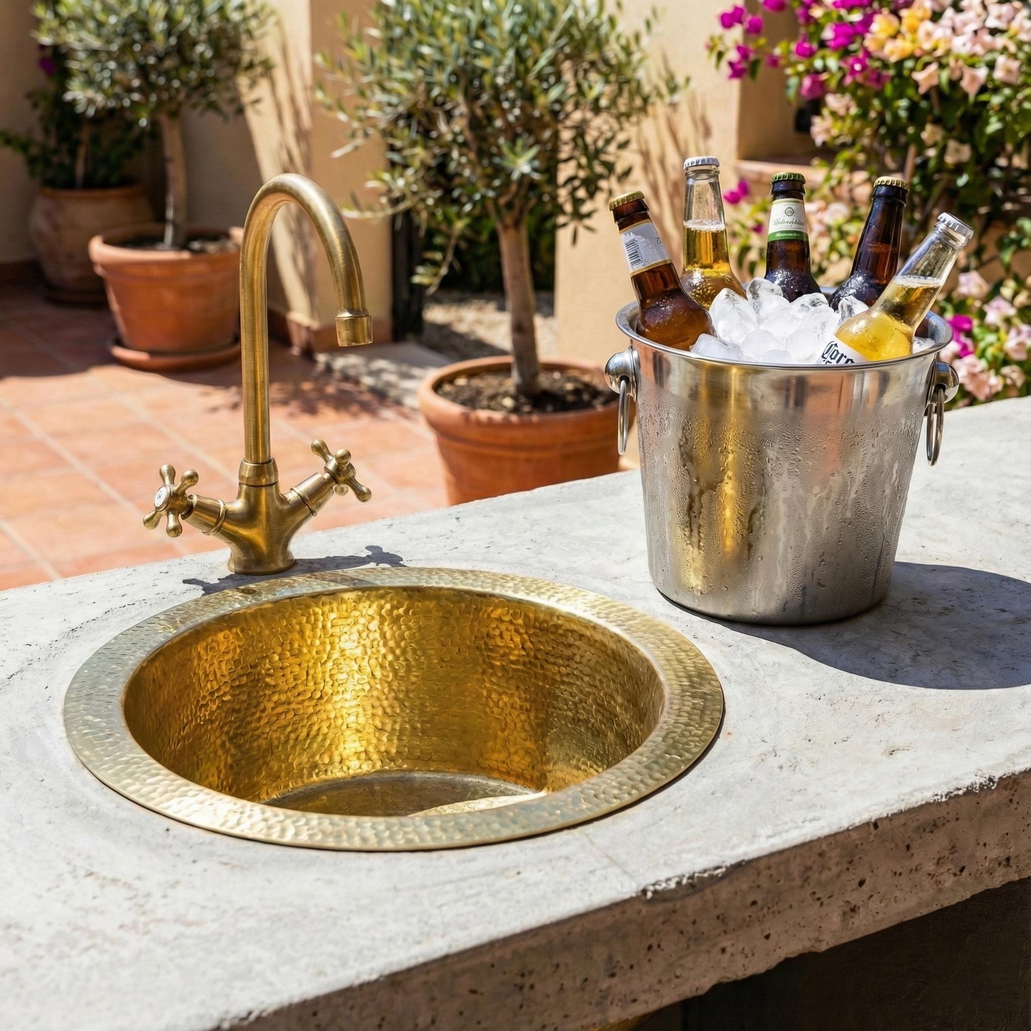 Gold sink on a concrete surface with a bucket of ice and bottles in an outdoor setting.