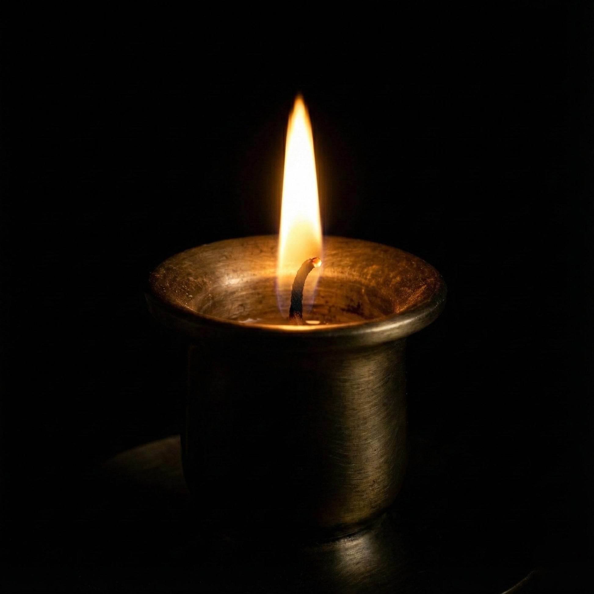 Candle in a metal holder with a single flame against a black background
