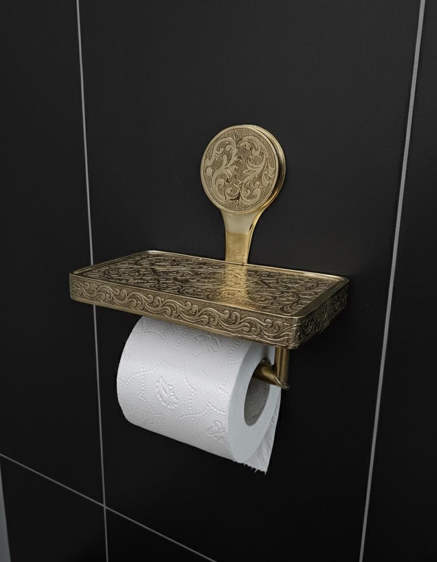 Decorative brass toilet paper holder on a black tiled wall