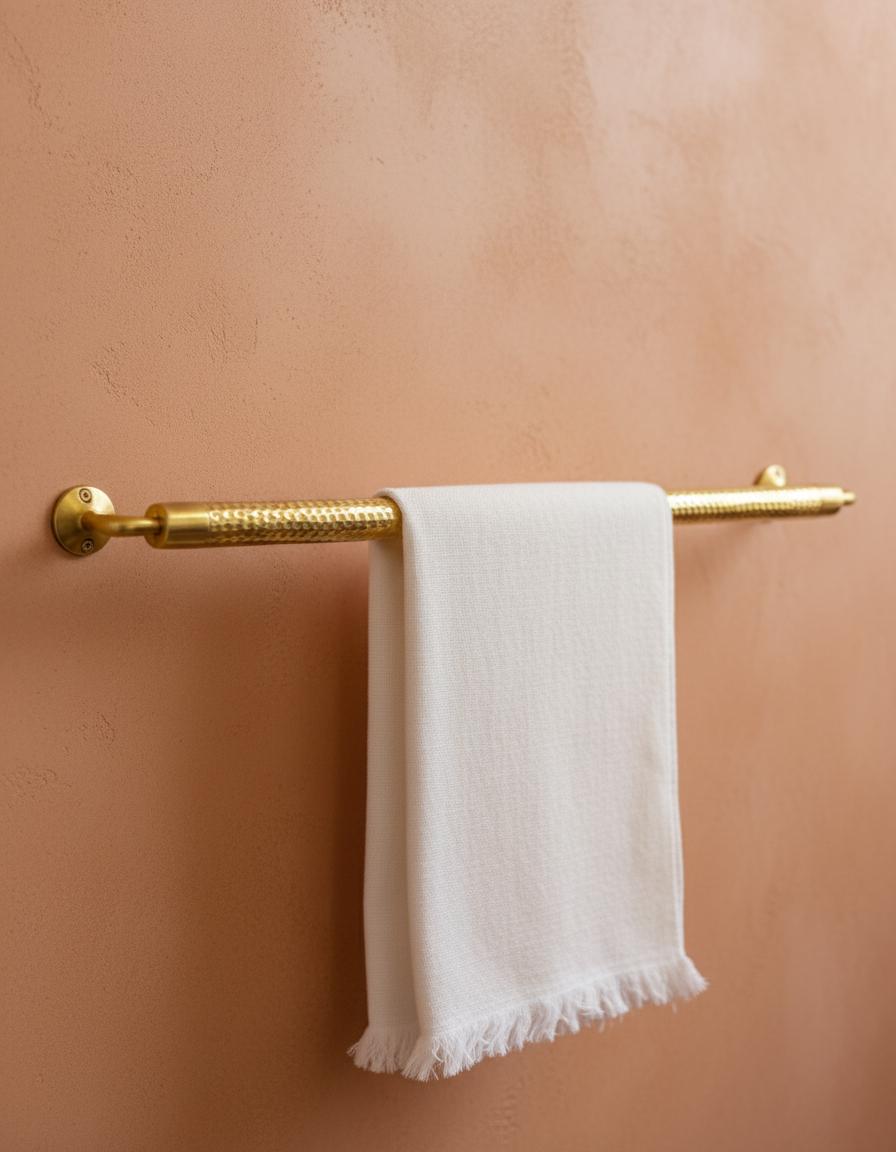 Gold towel rack with a white towel on a peach-colored wall