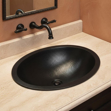 Black oval sink on a beige countertop with a bronze faucet.