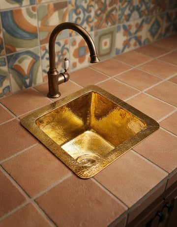 Gold sink with bronze faucet on a tiled countertop with patterned backsplash