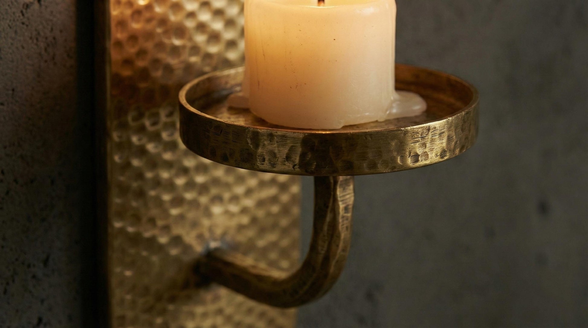 Candle in a brass wall-mounted holder against a textured wall.