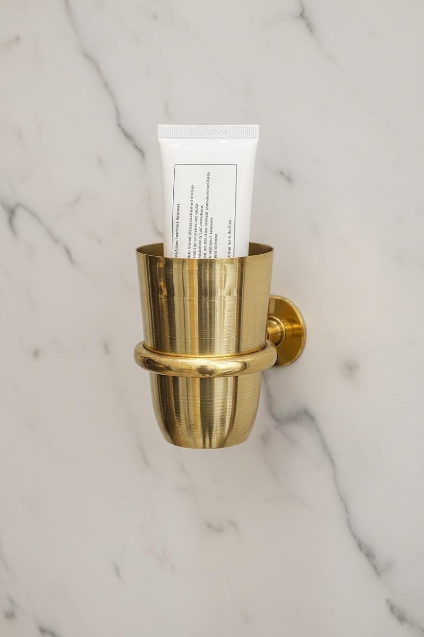 Gold wall-mounted holder with a tube of toothpaste on a marble background