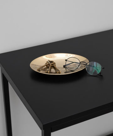 Gold decorative plate with a sculpture and eyeglasses on a black surface