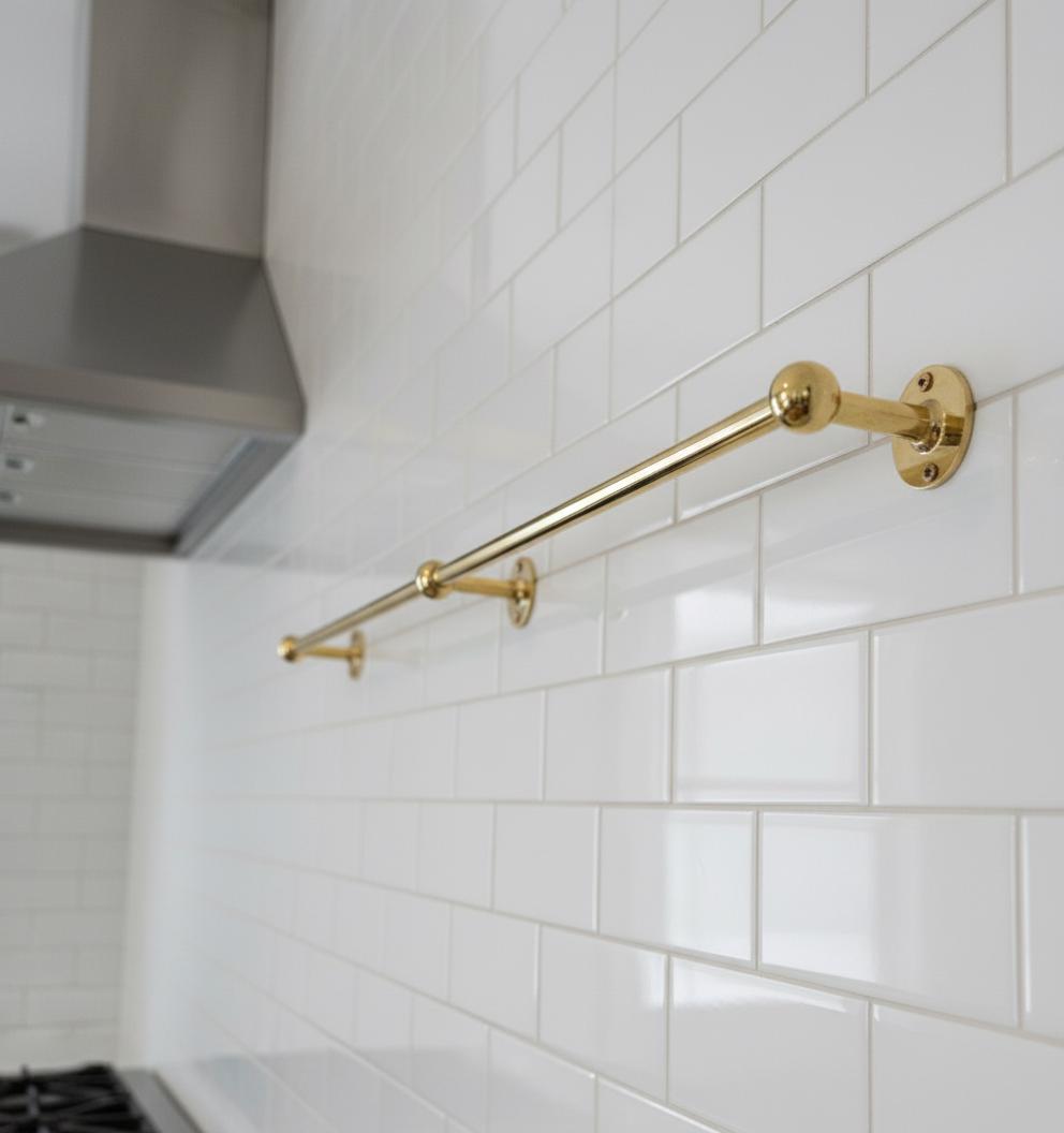 Gold towel bar mounted on a white tiled wall in a kitchen.