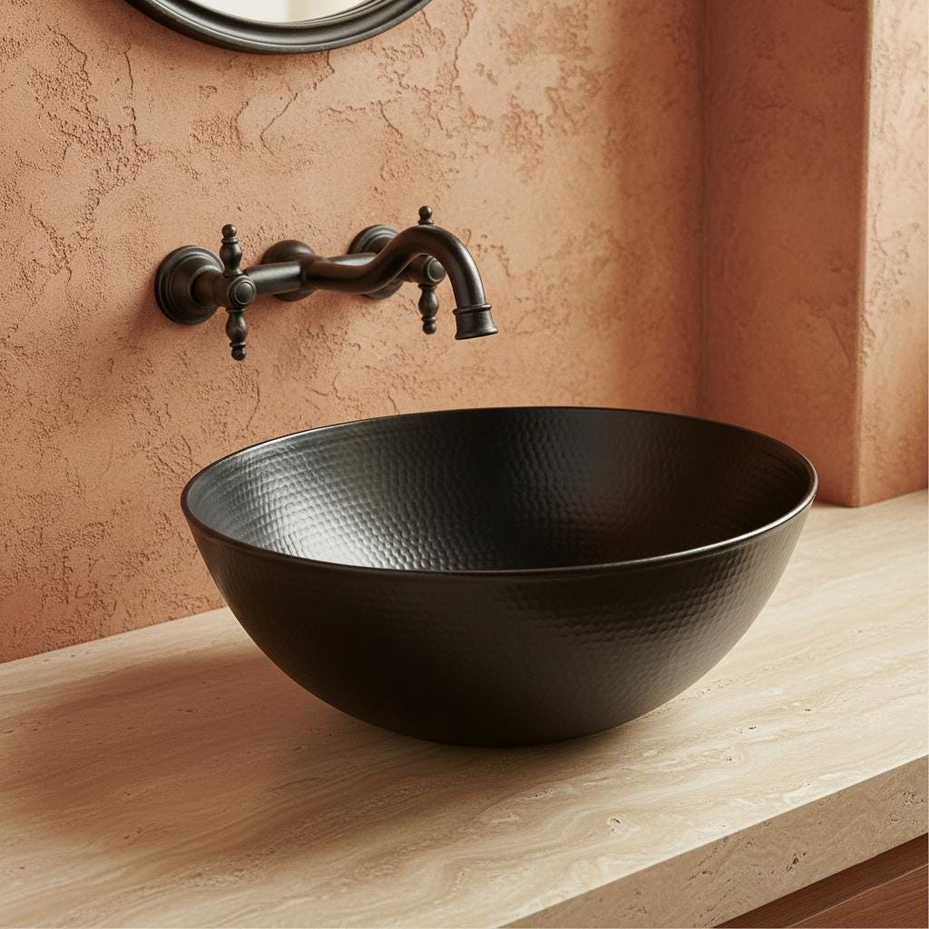 Black hammered sink on a wooden countertop with bronze faucet against a textured wall.