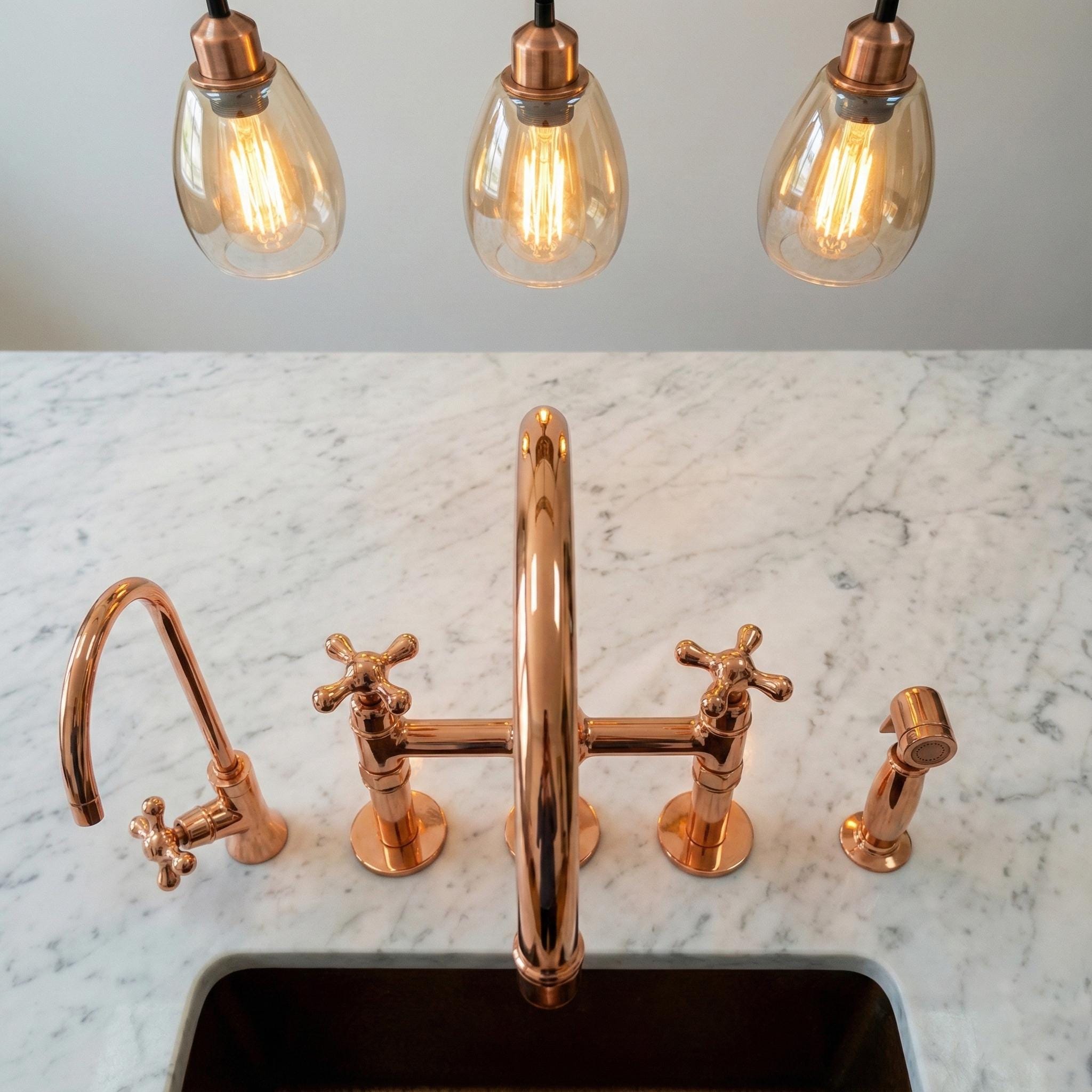 Rose gold faucet set on a marble countertop with pendant lights in the background.
