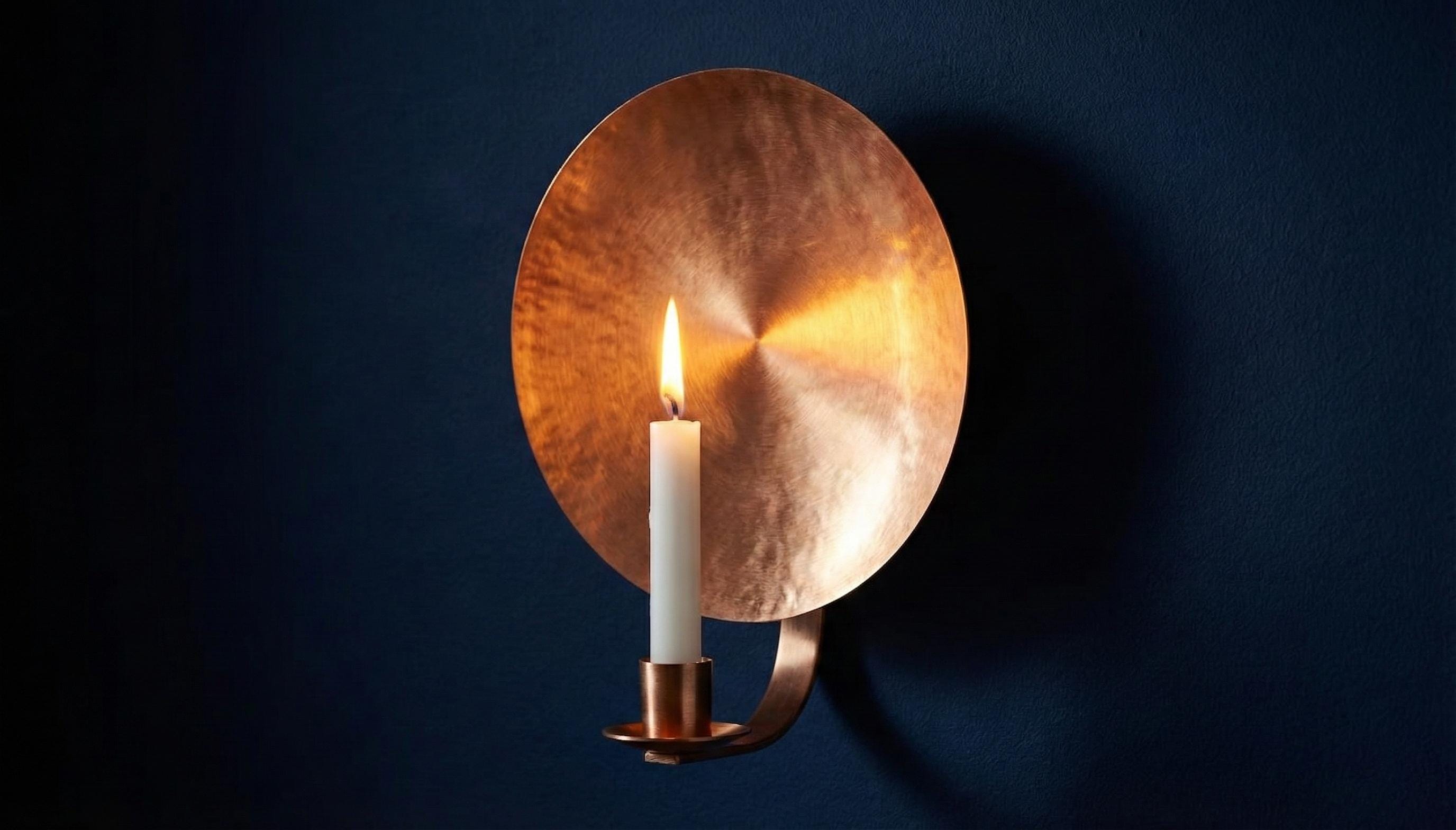 Copper wall sconce with a lit candle against a dark background