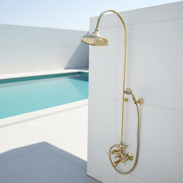 Gold shower set mounted on a white wall with a pool in the background