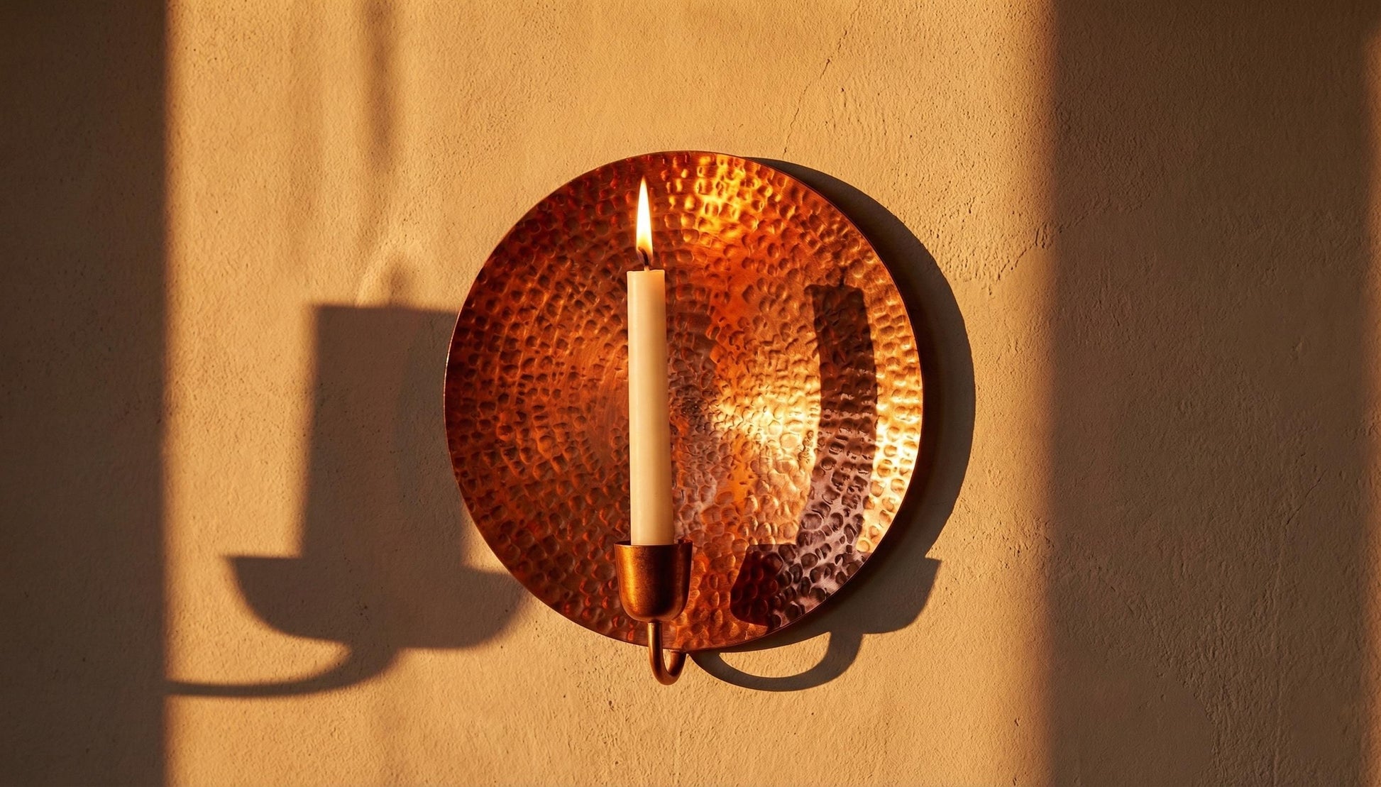 Candle in a copper holder on a beige wall