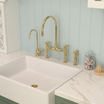 Gold kitchen faucet and handles on a white sink with a light blue wall in the background.
