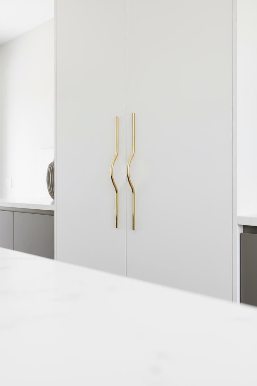 Hand opening a white cabinet door with gold handles.
