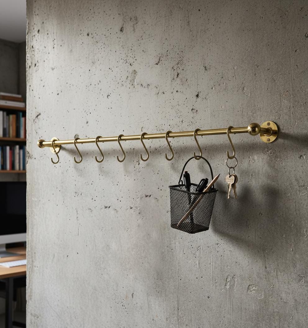 Brass hook rack mounted on a concrete wall with a small basket and keys hanging from it.