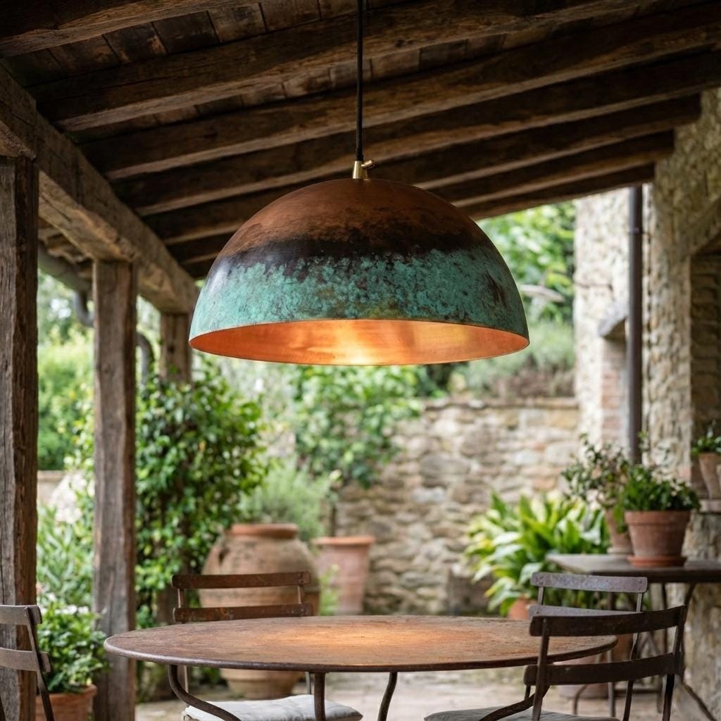 Rustic pendant light hanging above a wooden table in an outdoor setting with stone walls and greenery.