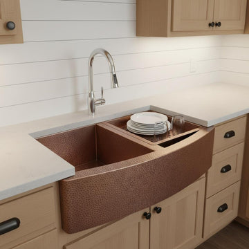 Brown farmhouse sink in a kitchen with white tiled wall and wooden cabinets.