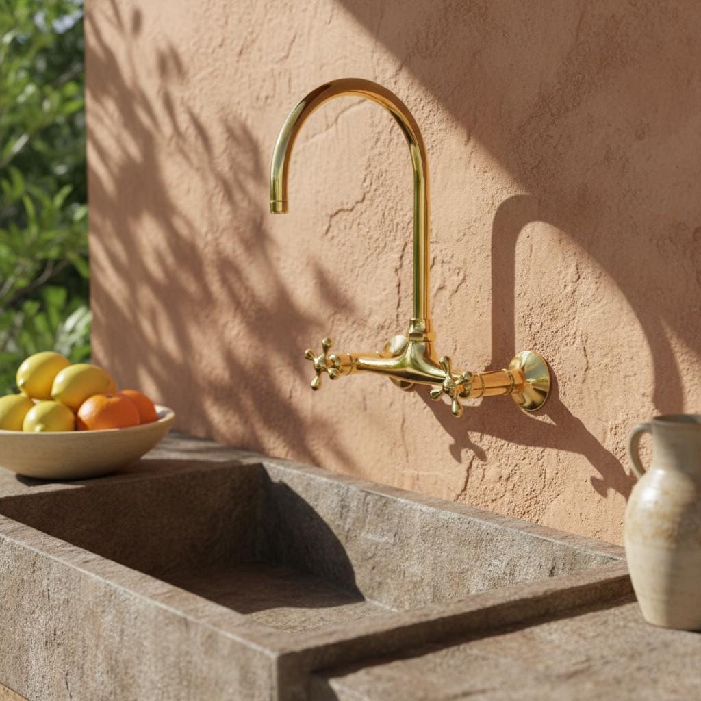 Gold faucet on a stone sink with a bowl of fruit and a vase in the background.