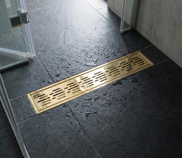 Gold floor drain cover on a dark tiled bathroom floor.
