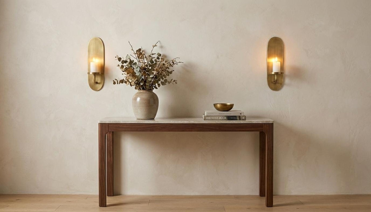 Wooden console table with decorative items against a beige wall with wall sconces.
