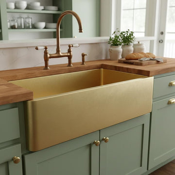 Gold farmhouse sink in a kitchen with wooden countertops and green cabinets.