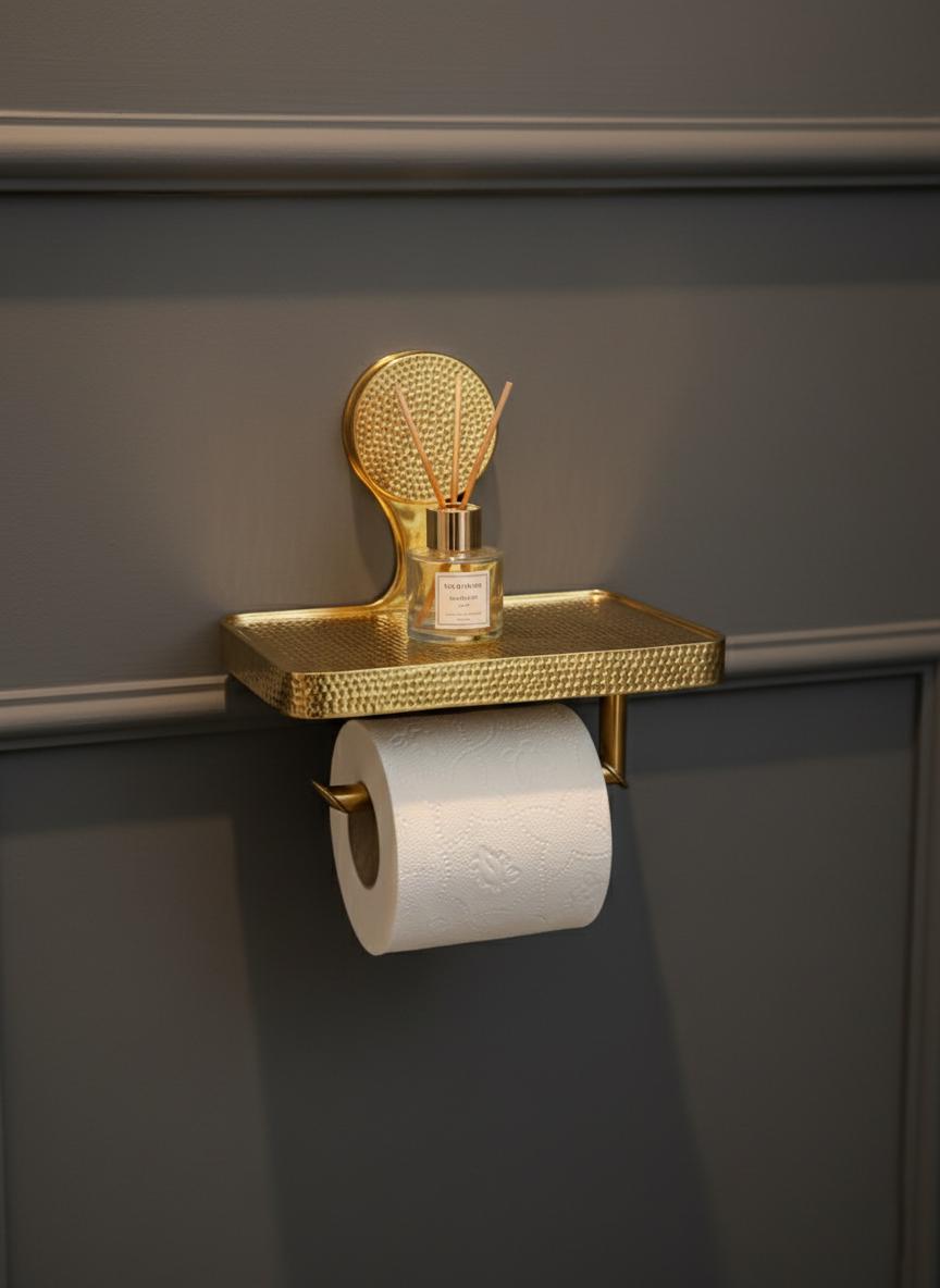 Gold decorative shelf with a small bottle and roll of toilet paper against a dark wall.