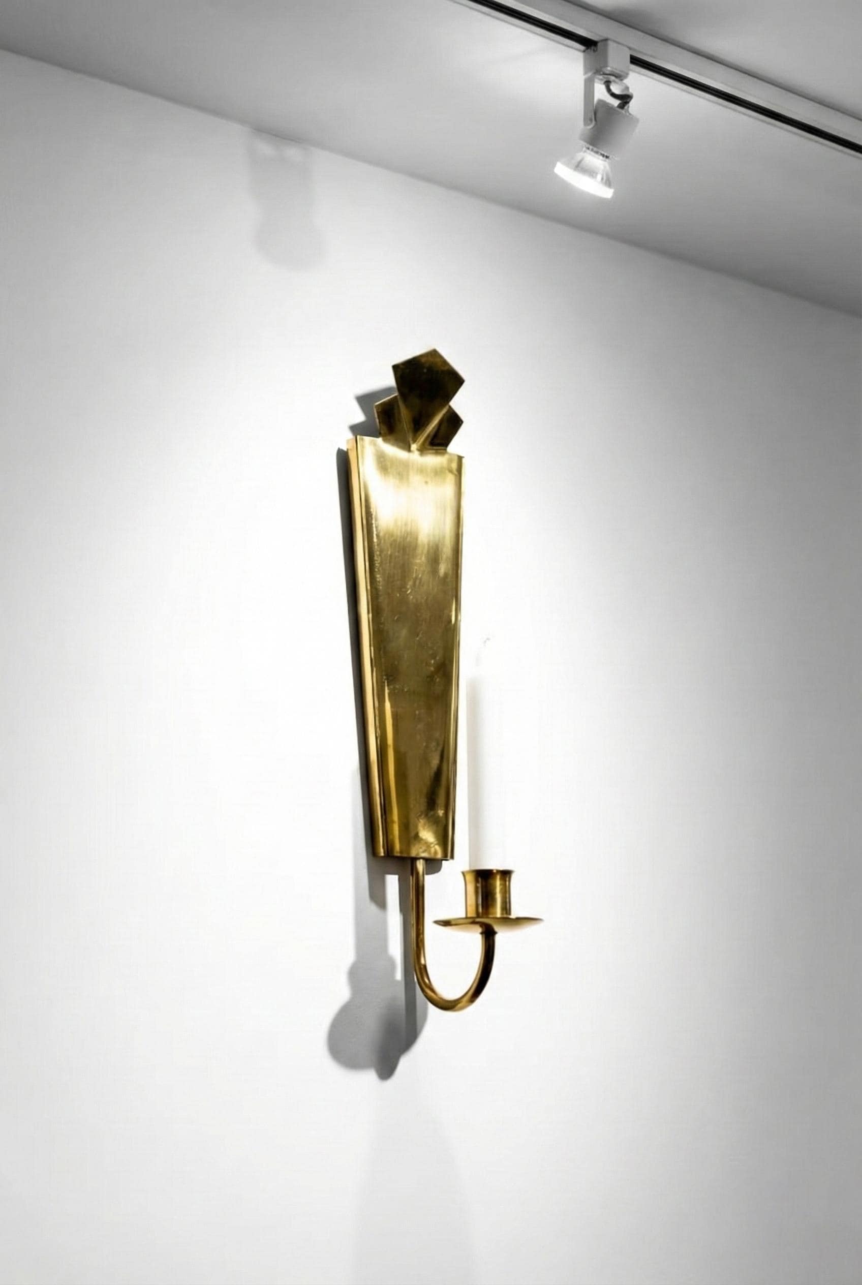 Gold wall sconce on a white wall with a spotlight above