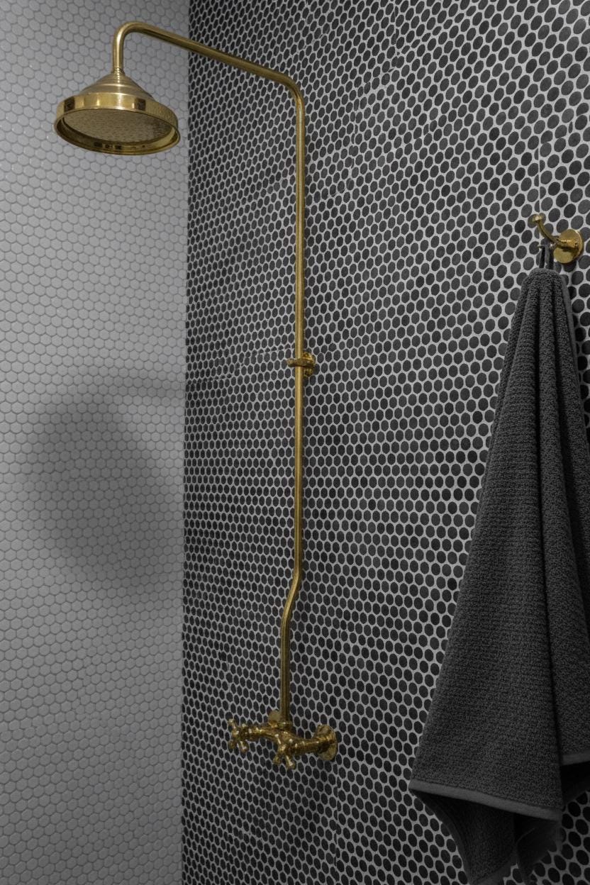 Gold shower head and hose against a patterned wall with a towel hanging on a hook.