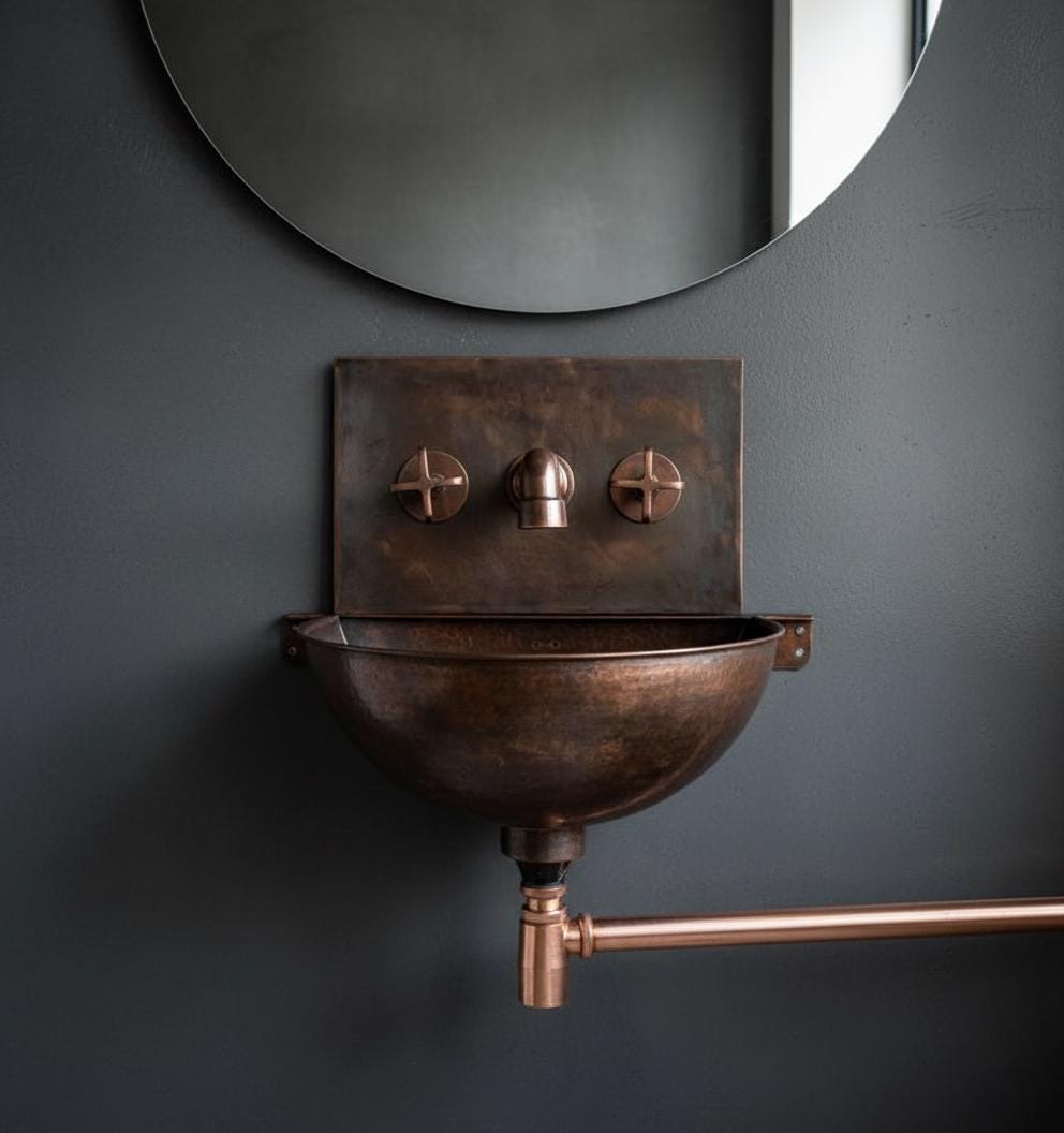 Bronze wall-mounted sink with copper fixtures against a dark gray wall.