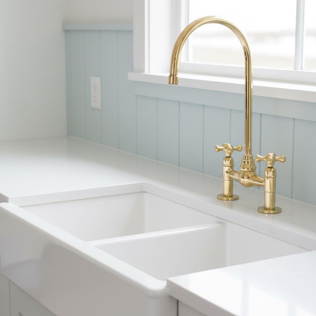 Gold kitchen faucet on a marble countertop with a light gray wall background