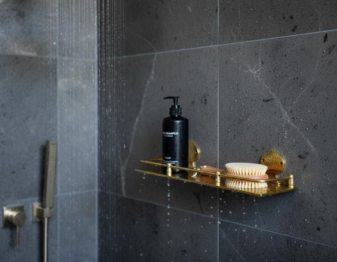 Shower area with a gold soap dish holding a black bottle and a white brush against a dark tiled wall.