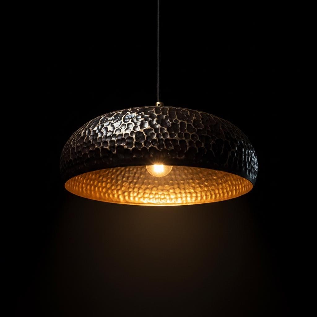 Hammered metal pendant light with a dark and gold finish on a black background