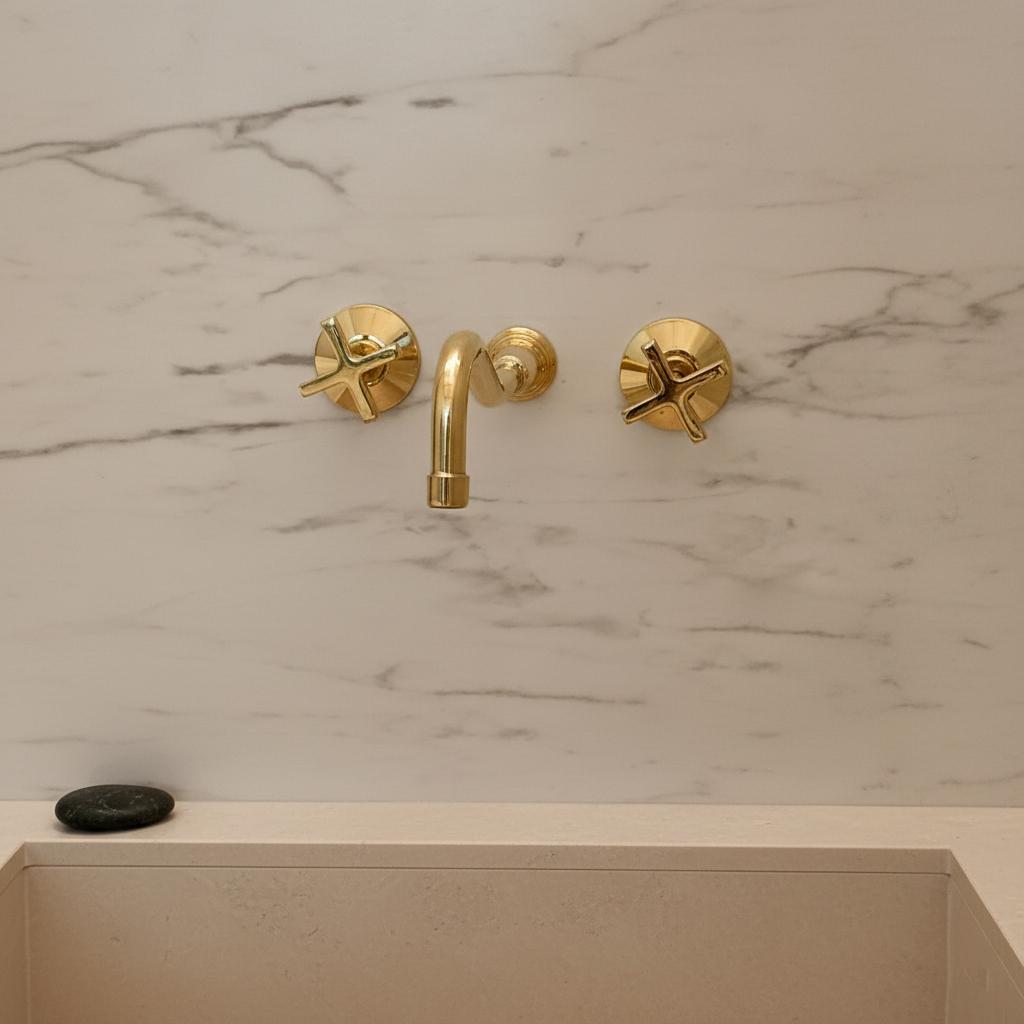 Gold faucet and handles on a marble wall with a beige sink.