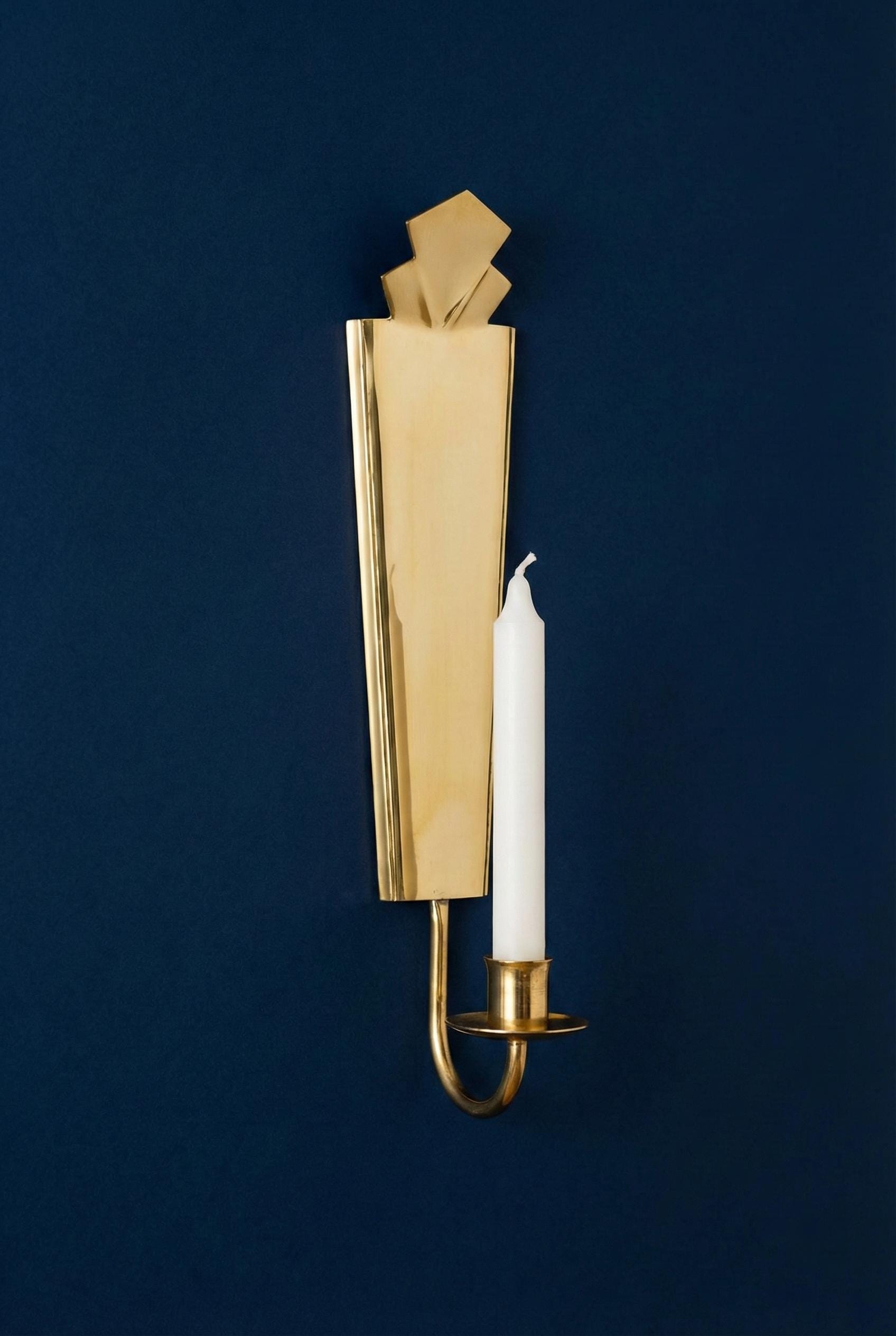 Gold wall sconce with a white candle against a dark blue background