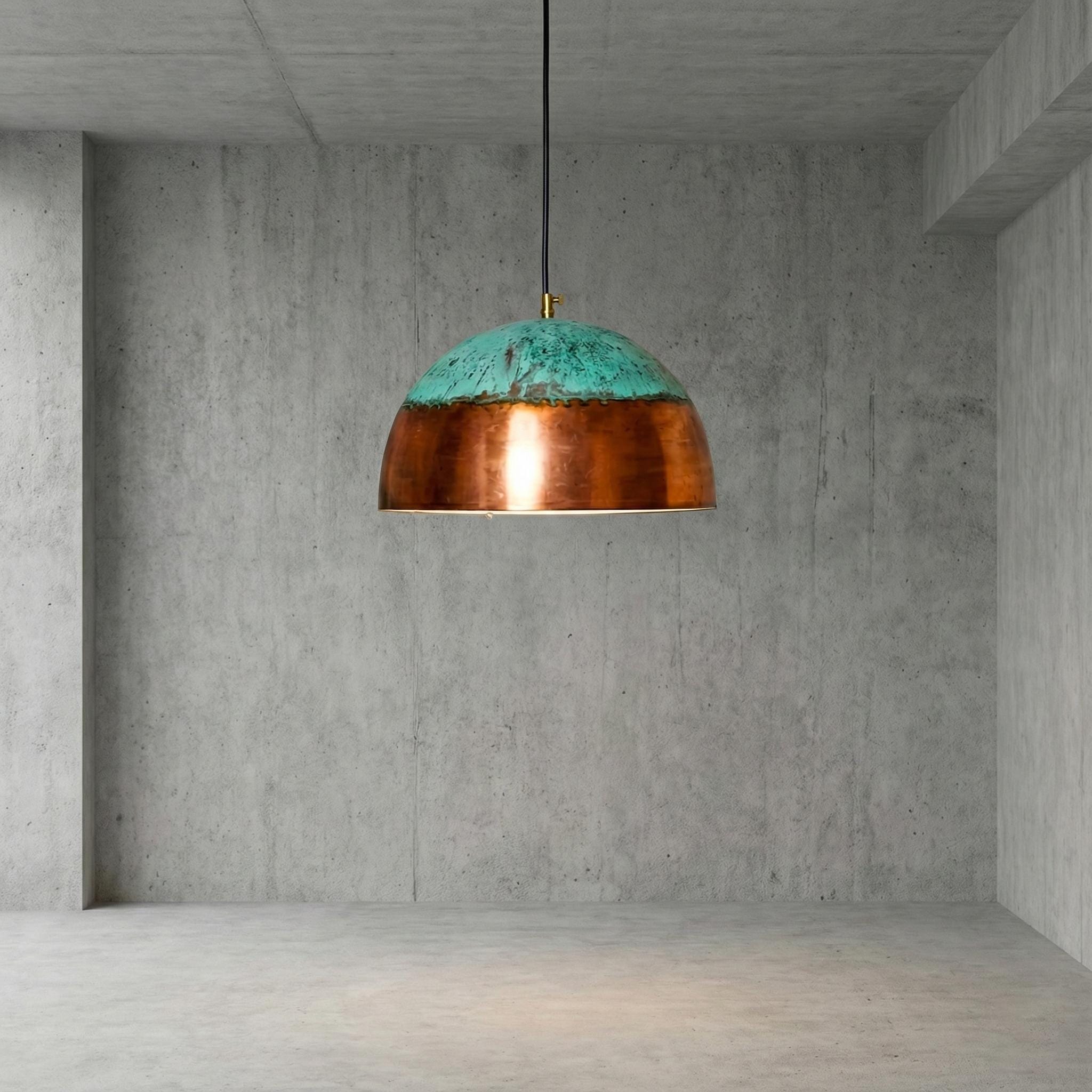 Pendant light with copper and teal design hanging in a concrete room.